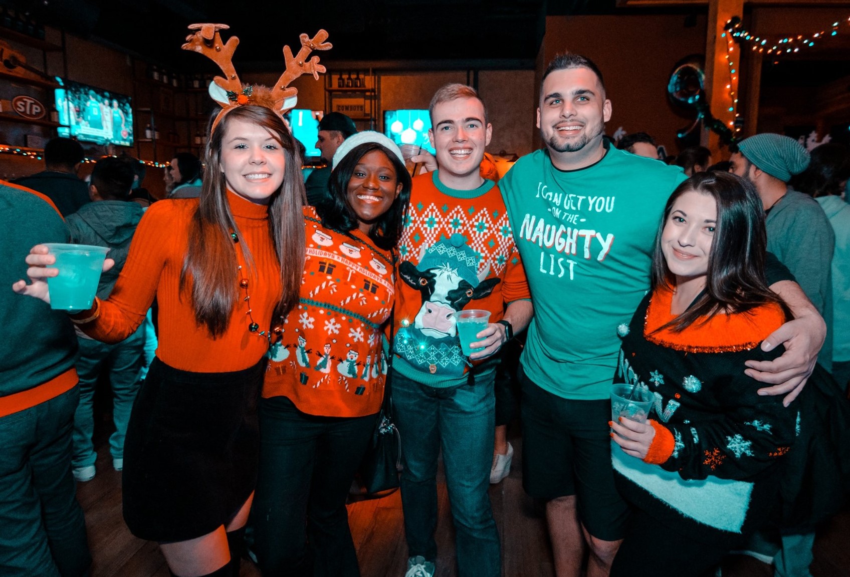 Three men and two women dressed for holiday ugly sweater party at a bar.