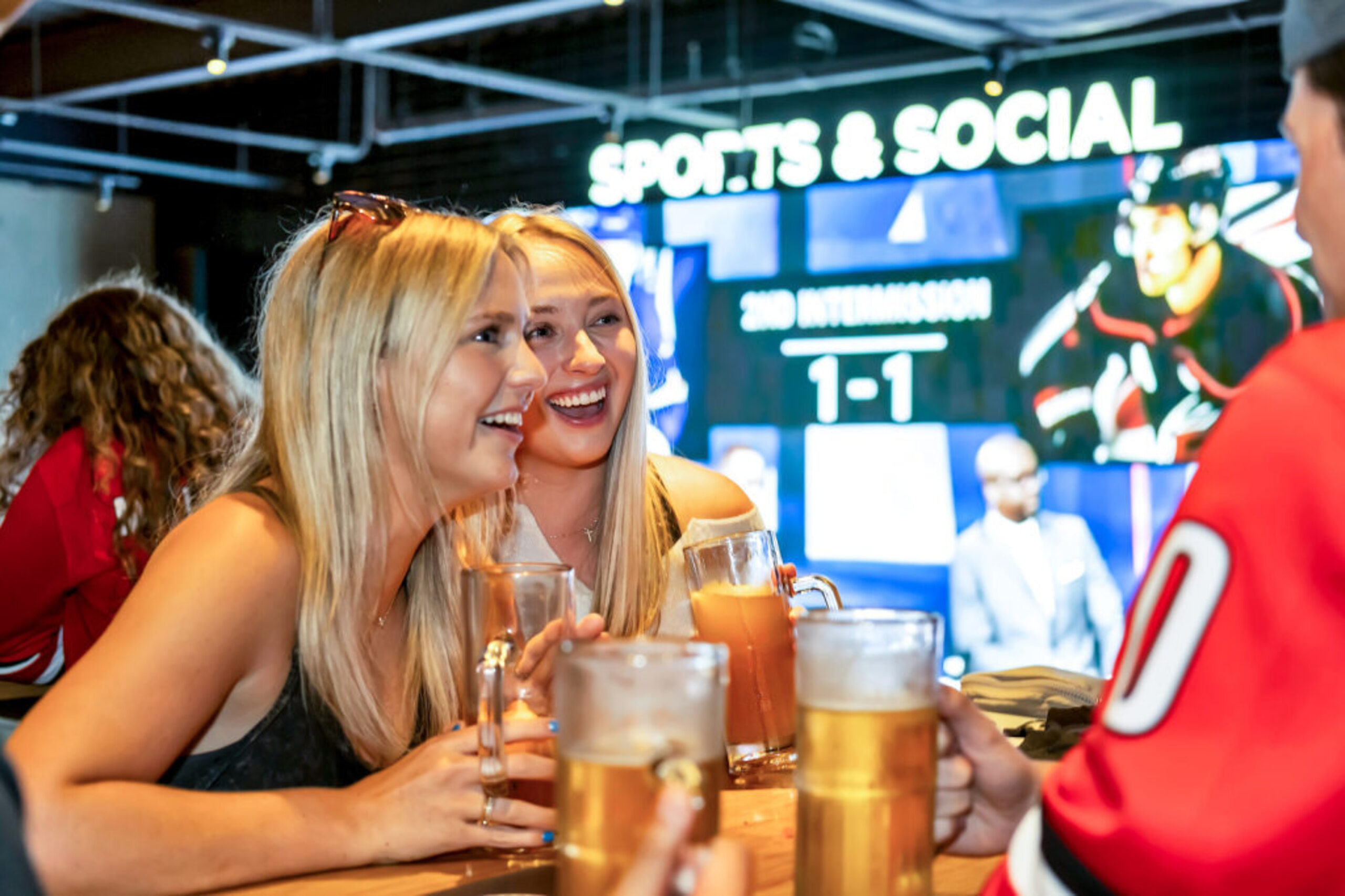 Two women enjoying beers and watching hockey at Sports & Social in Cary, NC.