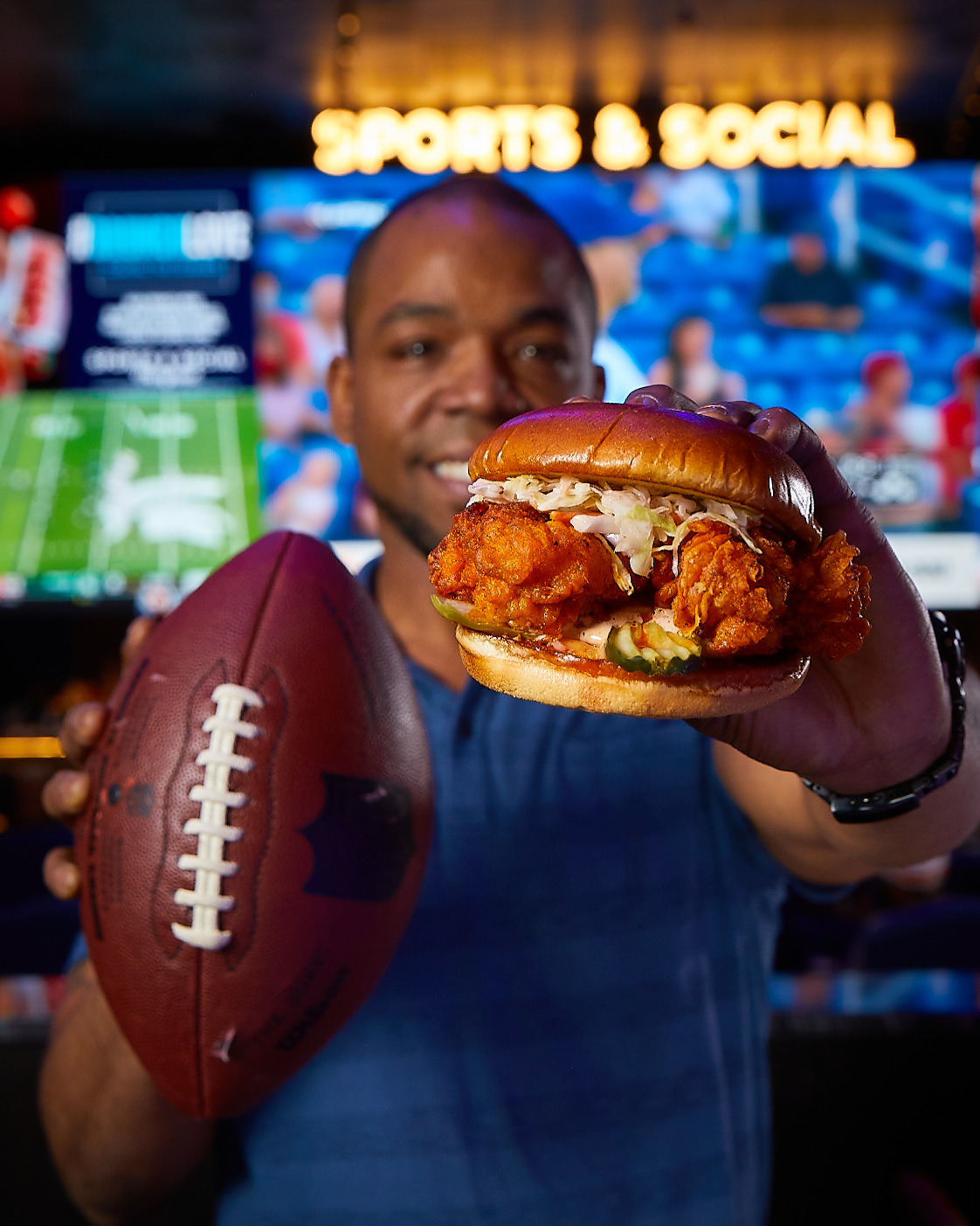 Man at Sports & Social holding a football and a Nashville Hot Chicken Sandwich.