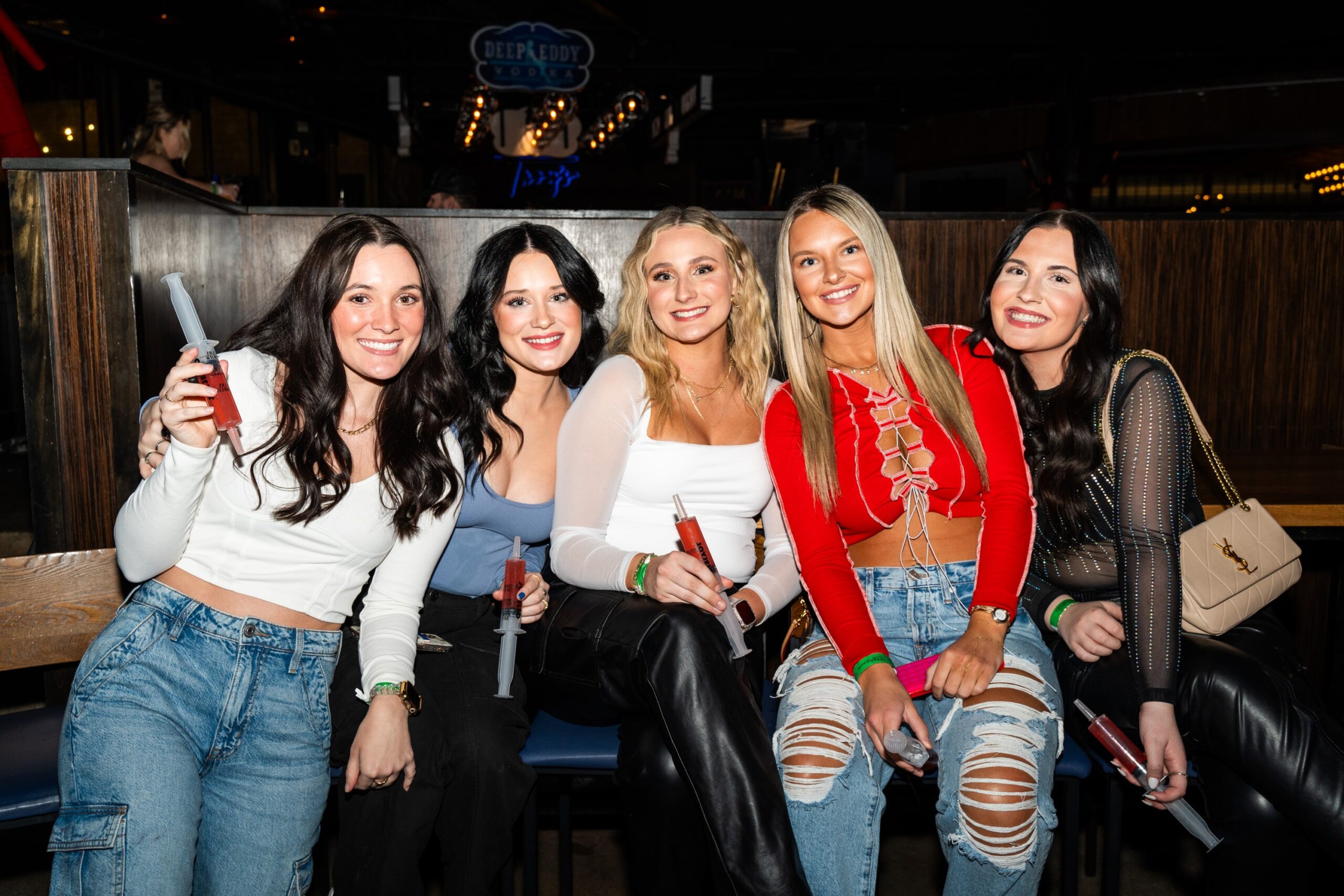 Five women in a booth at Sports & Social drinking shots in syringes.