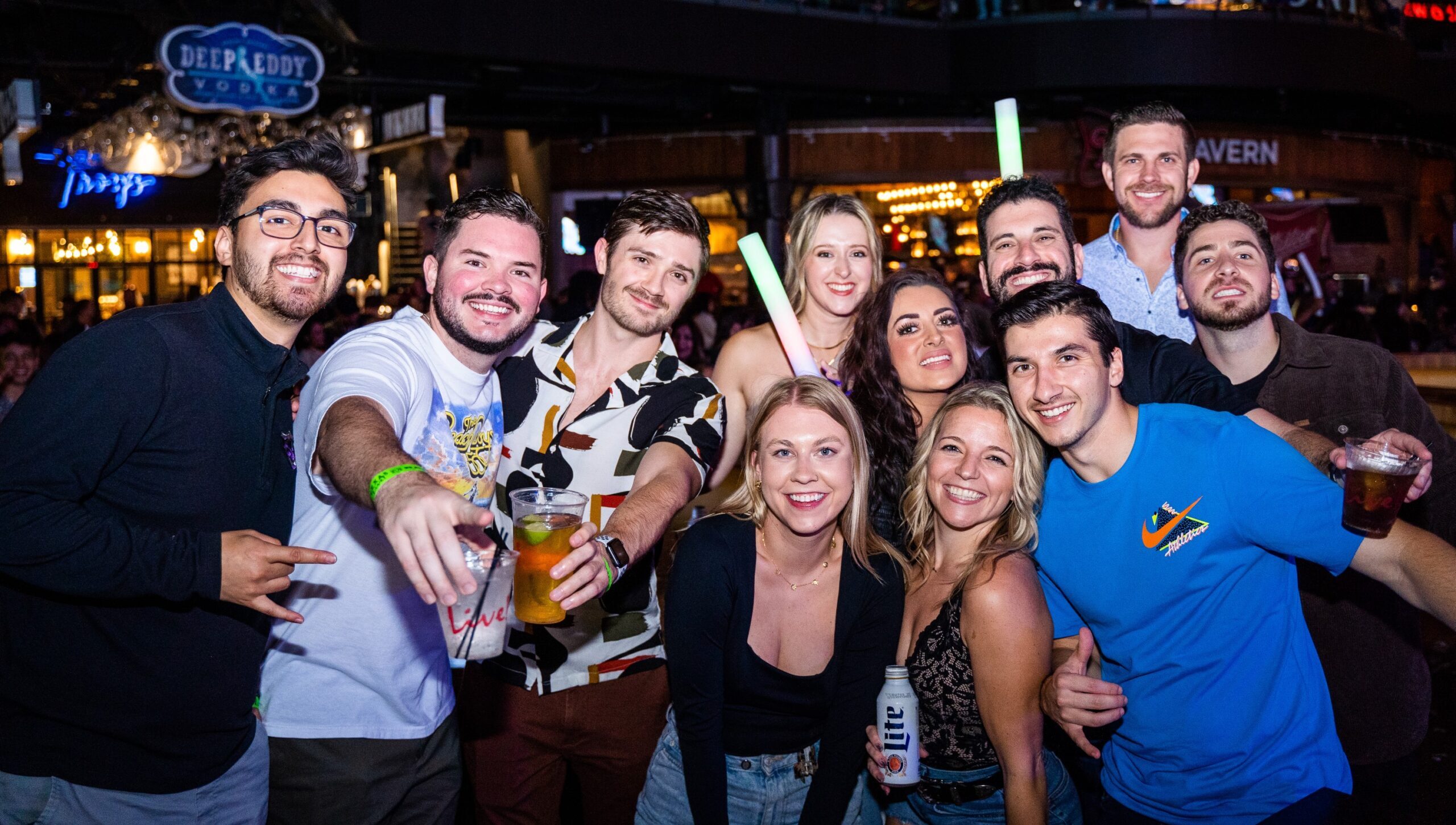 Group of men and women with drinks at Sports & Social sports bar.